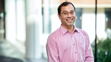 Amit smiles towards the camera. He is wearing a pink shirt.