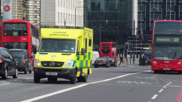 An image of an ambulance on a London road, with cars and double-decker buses in the background
