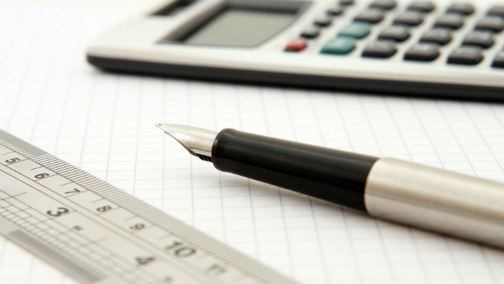 A metal ruler, fountain pen and calculator on top of squared paper.