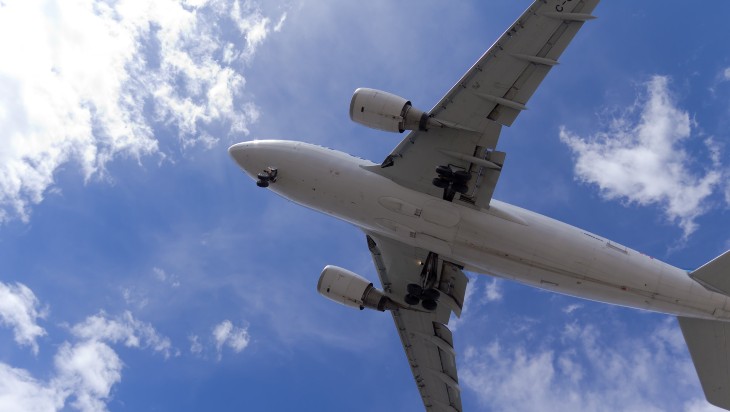 A passenger airplane in flight, viewed from below. The sky is blue with white, whispy clouds.