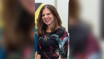 Rosalind, who has shoulder length brown hair and is wearing a black floral top, smiles toward the camera