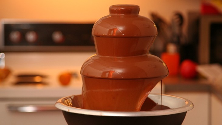 A chocolate fountain in the foreground. A cooker and kitchen worktop are out of focus in the background.