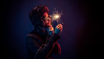 Innovators of the Future: The IMA / BCS / IET Christmas Lecture A person in a "thinking pose" holding a sparker. The image is dark, with the only illumination from the sparklr.
