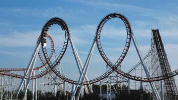 Image of a white and black rollercoaster with three loops and a blue sky in the background